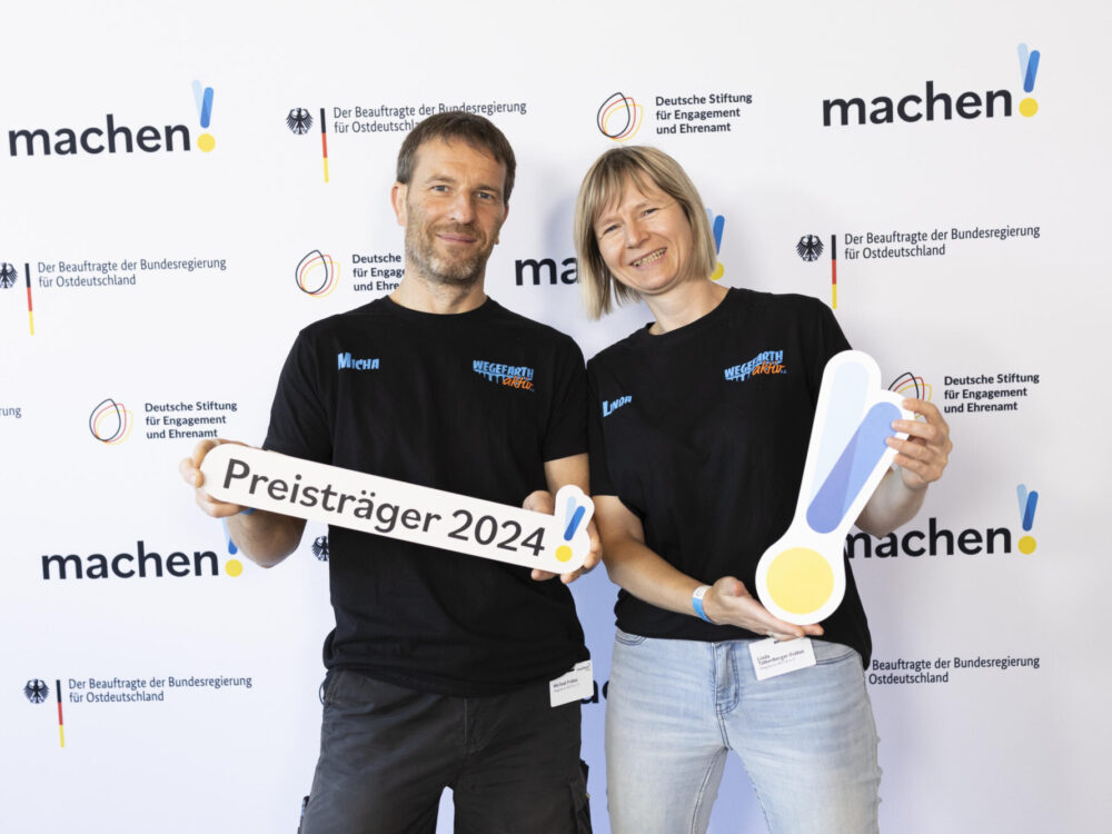 Ein Mann und eine Frau halten die Auszeichung der Preisverleihung von „machen!2024“ in die Kamera.