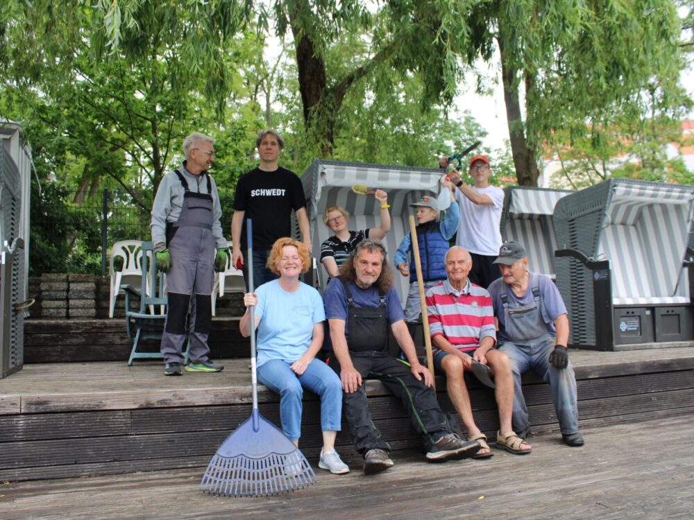 Gruppenfoto von ehrenamtlichen Helfern mit Besen, Rechen und Arbeitskleidung.