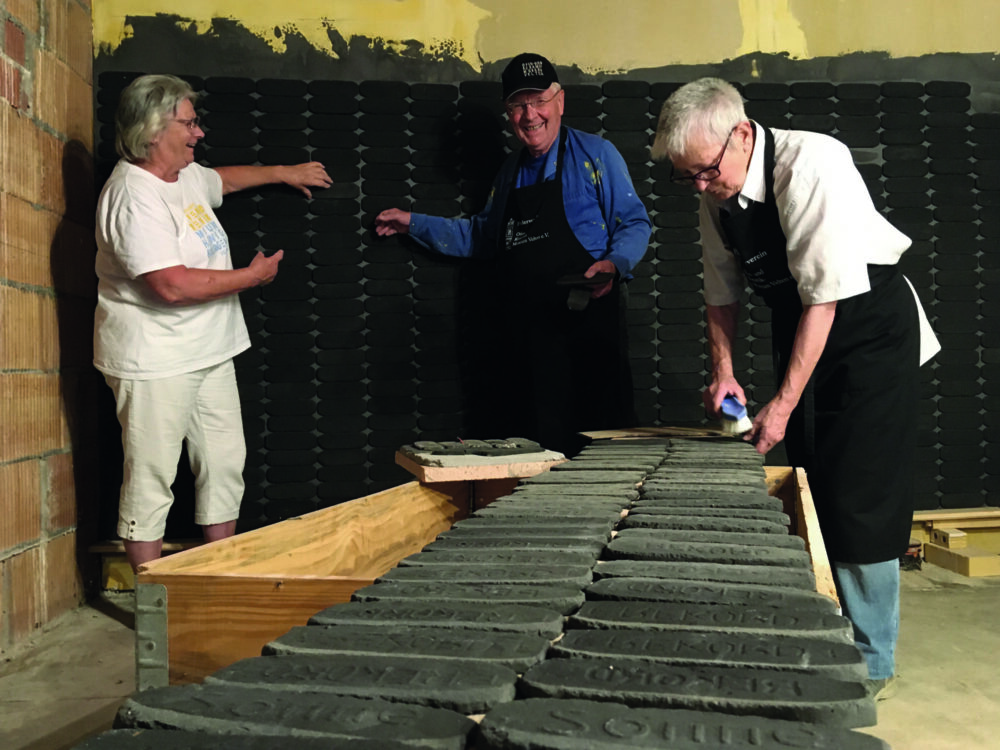 Drei ältere Menschen präsentieren und reinigen alte Kacheln in der Ofenfabrik.