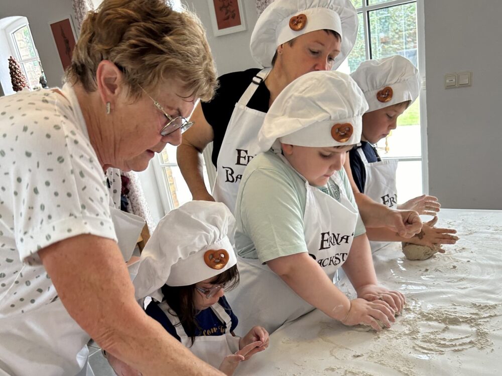 Zwei Frauen kneten mit drei Kindern mit Bäckermützen Teig.