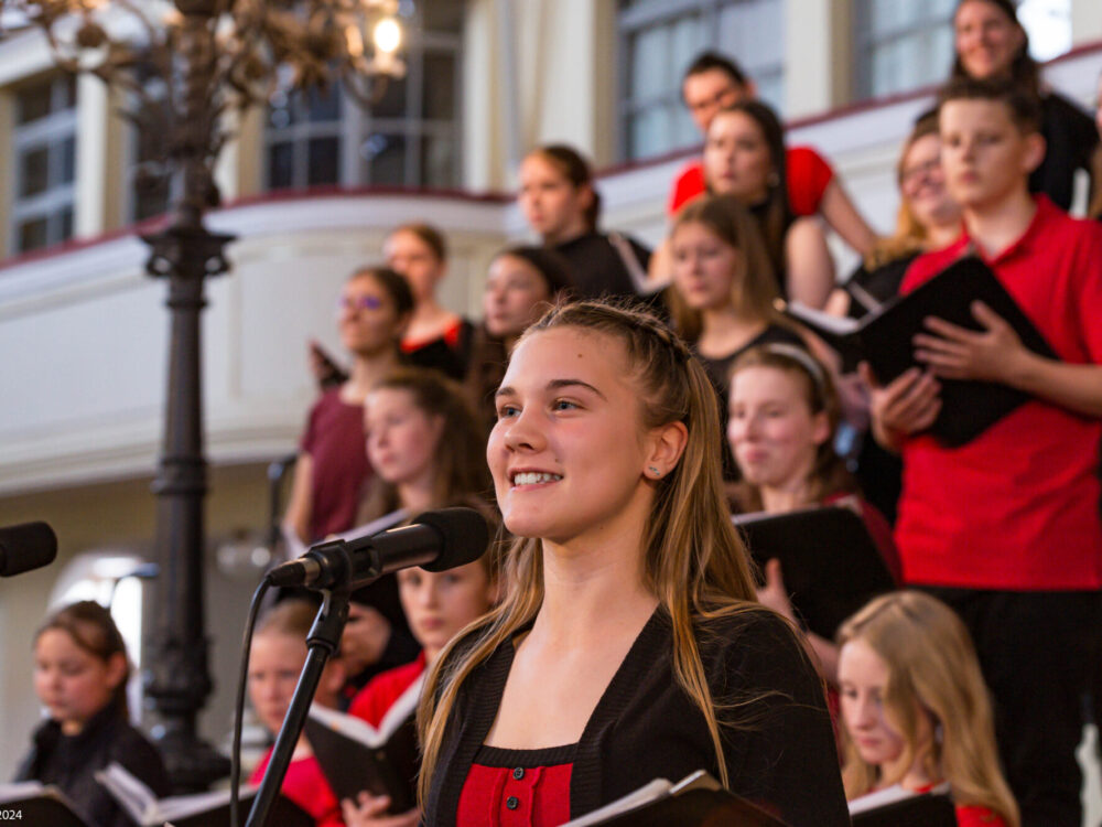 Ein Jugendchor singt in einer Kirche. Im Vordergrund singt ein Mädchen ein Solo am Mikrofon.