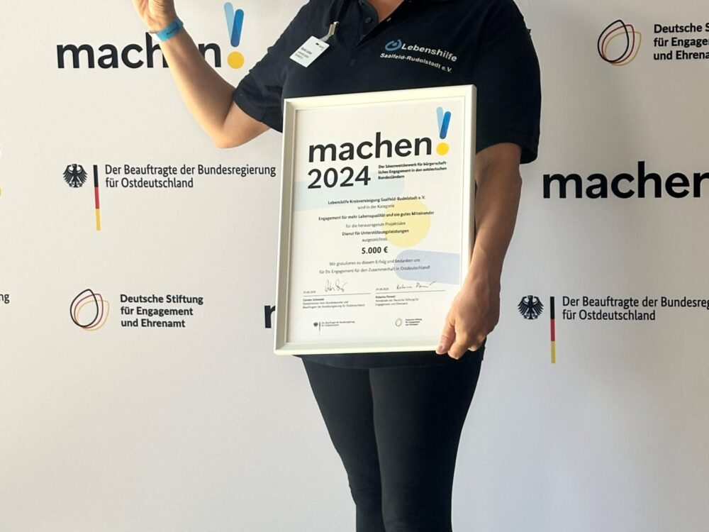 Eine Frau hält die Auszeichung der Preisverleihung von „machen!2024“ in die Kamera.