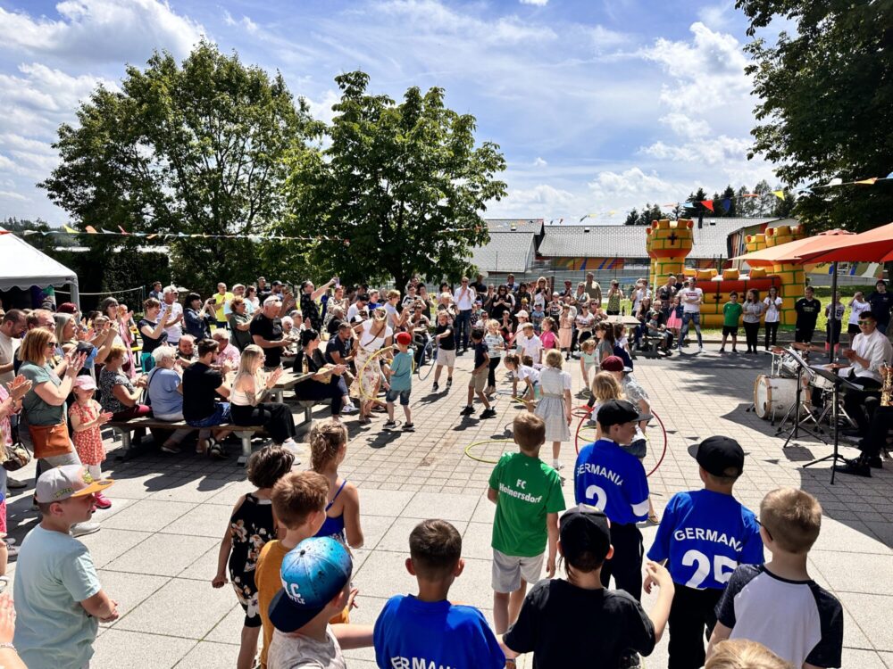 Kinder spielen Hula Hoop auf einem gut besuchten Sommerfest.