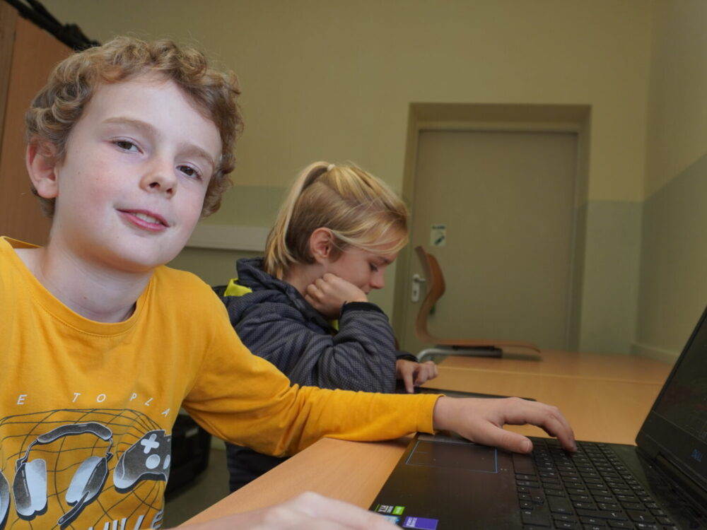 Zwei Jungen sitzen an einem Schreibtisch mit Tablet und Laptop.