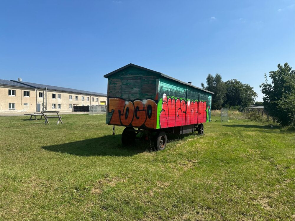 Ein bunter Bauwagen steht auf einer Wiese. In Graffiti-Buchstaben steht darauf „ToGo Jugendclub“.