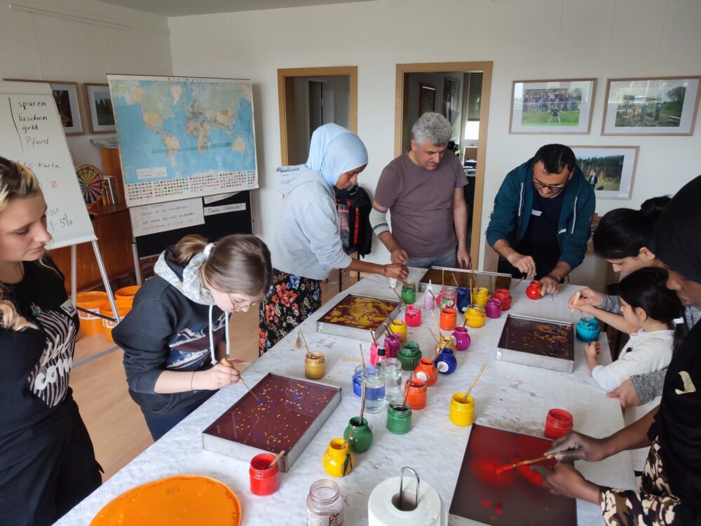 Eine Gruppe von Kindern und Erwachsenen steht um einen Tisch und malt Bilder.