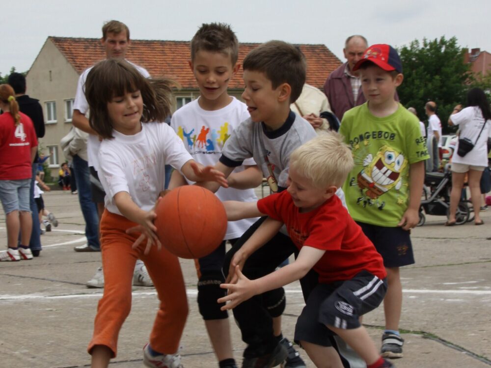 Kinder spielen mit einem Basketball auf einem Dorfplatz.