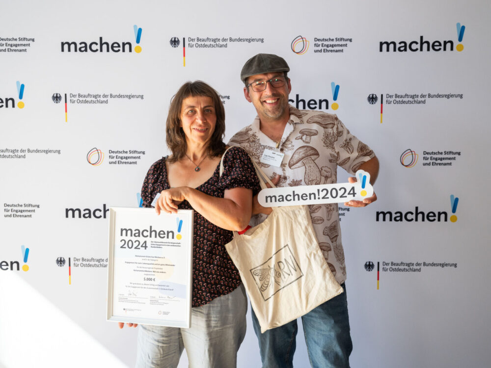 Ein Mann und eine Frau halten die Auszeichnung der Preisverleihung von „machen!2024“ in die Kamera.