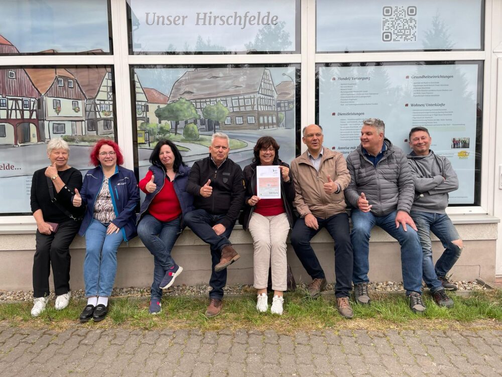 Eine Gruppe von Menschen sitzt auf einer Mauer und strahlt fröhlich in die Kamera.