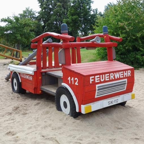 Ein Spielfeuerwehrauto aus Holz steht auf einem Spielplatz im Sand.