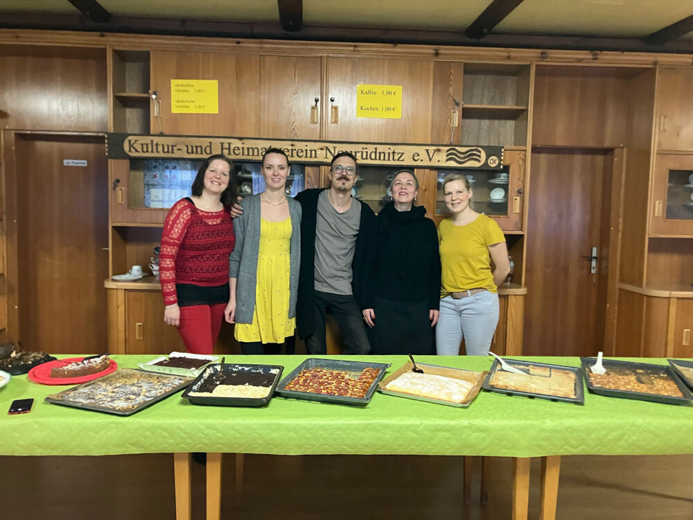 Fünf Menschen posieren hinter einem Kuchenbuffet.