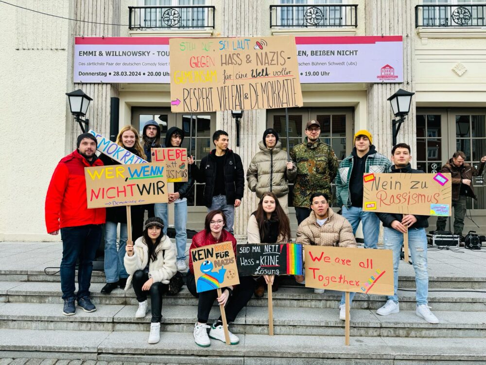 Gruppenfoto von Jugendlichen mit beschrifteten Pappschildern. Zu lesen ist unter anderem „Nein zu Rassismus“, „Demokratie“ und „Wer, wenn nicht wir“.